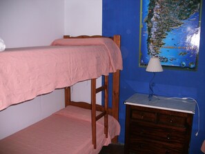 A bunk bed with a pink blanket, a small wooden dresser, and a map on the wall. - Hostel Playa (Villa Gesell)