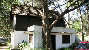 Un bâtiment à deux étages, avec un toit recouvert de tuiles, un grand arbre devant et une voiture rouge garée  à proximité.
