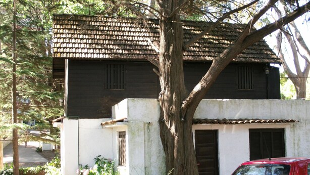 Un edificio de dos pisos con techo de tejas y un árbol grande en frente.