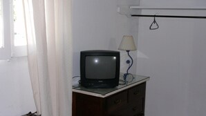 Une pièce avec une télévision posée sur une commode, une lampe et une fenêtre avec des rideaux.
