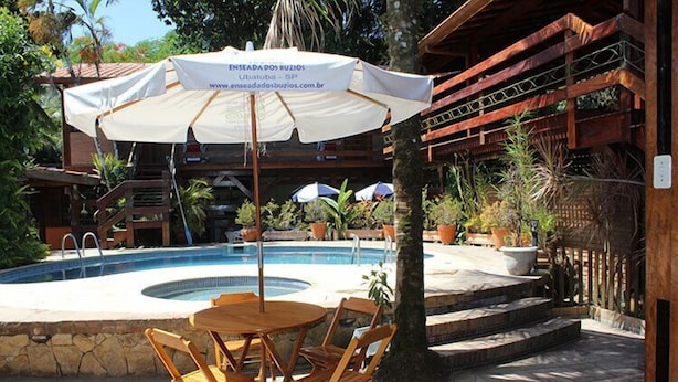A pool area with a wooden deck, a table with chairs, and a sign for 'Enseada dos Buzios'. - Pousada Enseada dos Búzios (Ubatuba)