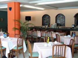 A restaurant with multiple tables and chairs, a large orange pillar, and decorative stained glass windows.