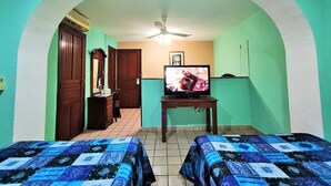 A room with two beds, a television on a stand, a ceiling fan, and a door leading to another room. - Novotel (Poza Rica)
