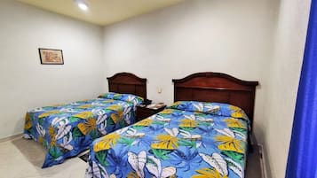 Una habitación con dos camas individuales, cada una con una colcha estampada, cabeceros de madera y una mesita de noche con lámpara.