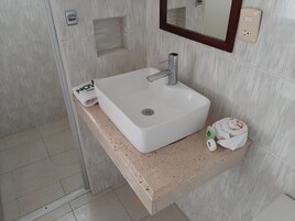 Un baño con un lavamanos blanco, un espejo y un perchero para toallas.