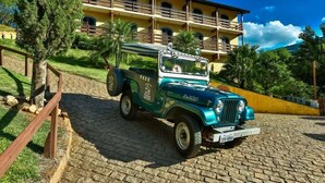 Une vieille jeep verte est garée sur un chemin pavé devant un bâtiment jaune doté de balcons.