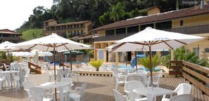 Un espace aménagé au bord de la piscine, avec des chaises et des parasols en plastique blanc, une terrasse en bois et une piscine en arrière-plan.