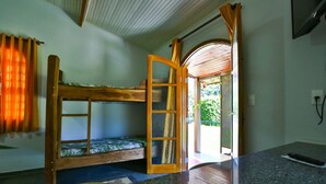 Un lit superposé avec une structure en bois et un panneau en verre, un petit coin salon avec un coussin et une télécommande posée sur un comptoir en granit.