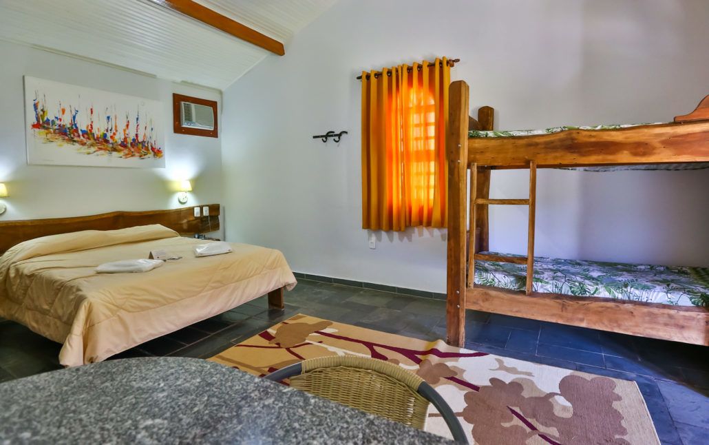 Una habitación con una cama nido, una cama individual, aire acondicionado montado en la pared, un cuadro y una alfombra estampada.