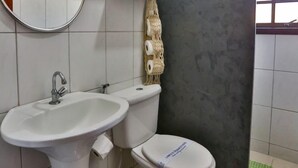 Une salle de bain avec un lavabo, des toilettes et un miroir. On y trouve également un porte-serviettes et une poubelle.