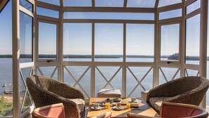 A conservatory with a panoramic view of a lake, furnished with wicker chairs and a table set for breakfast. - Costarenas Hotel & Spa (Colon)