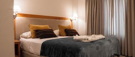 A neatly made bed with a dark blue blanket, two pillows, and a folded towel. There are two bedside lamps on either side of the bed.