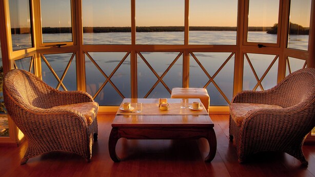 A room with wicker chairs, a wooden table, and a view of a body of water through large windows. - Costarenas Hotel & Spa (Colon)