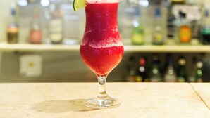 A cocktail in a glass with a lime garnish, set against a blurred background of various bottles. - Costarenas Hotel & Spa (Colon)