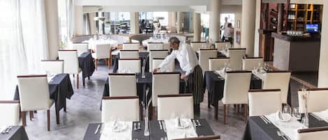 A restaurant with tables set for dining, a bar area, and a view of the outside.