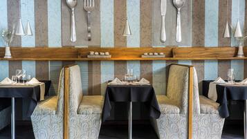 A restaurant with a modern interior, featuring striped wallpaper, hanging utensils, and uniquely designed chairs.