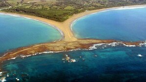 Vue aérienne d’une zone côtière avec une plage et des eaux d’un bleu limpide.