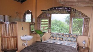 Une chambre à coucher comprenant un lit, une table de chevet, une commode, une fenêtre avec des volets en bambou, un lavabo fixé au mur et une armoire.