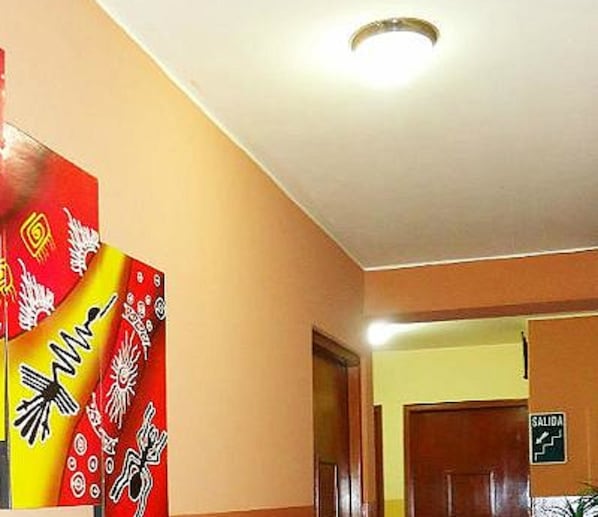 A hallway with a red and yellow patterned wall, a door with a 'SALIDA' sign, and a ceiling light.