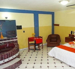 A hotel room with a large bed, a desk, a chair, a small table, and a bathtub.