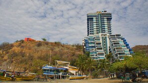 A tall hotel with multiple balconies, situated on a hillside with boats docked nearby. - Apartamentos Suiteline Master (Santa Marta)