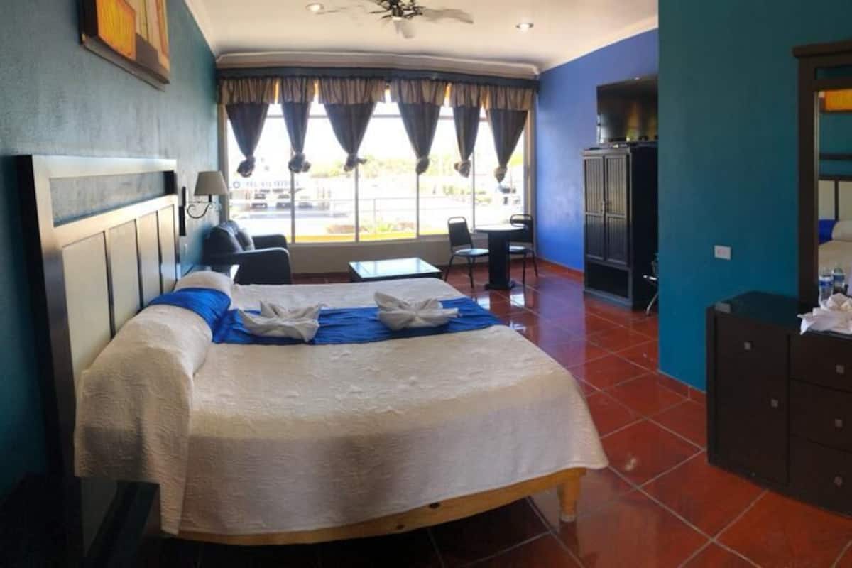 Una habitación de hotel con cama, escritorio, silla, armario y espejo.