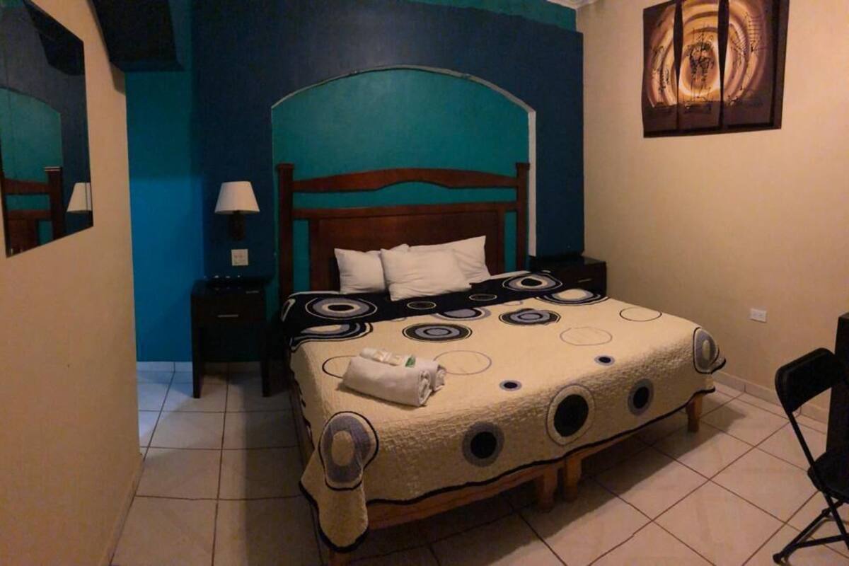 Un dormitorio con una cama, mesitas de noche, una silla y obras de arte en las paredes.