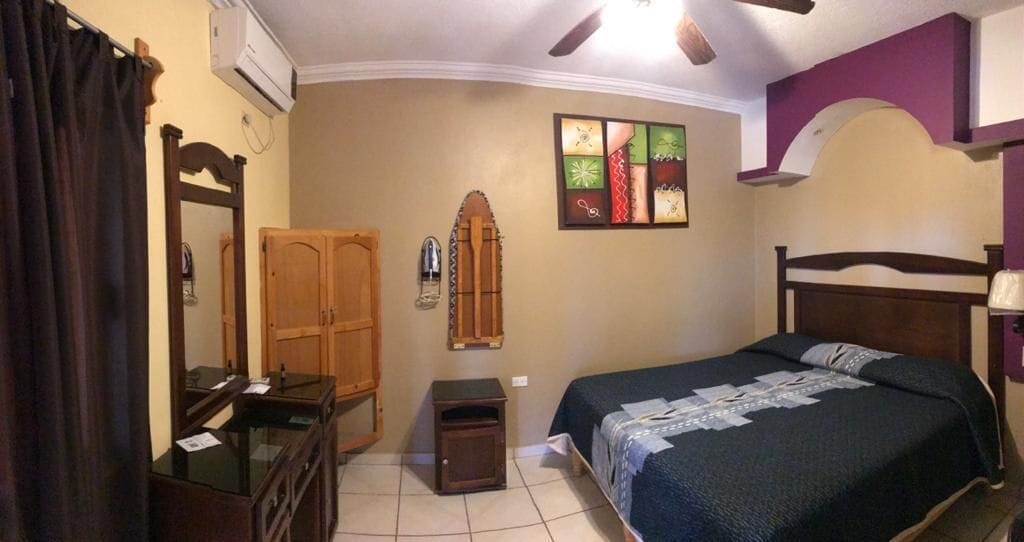 Un dormitorio con cama, cómoda, espejo, una mesita y aire acondicionado instalado en la pared.