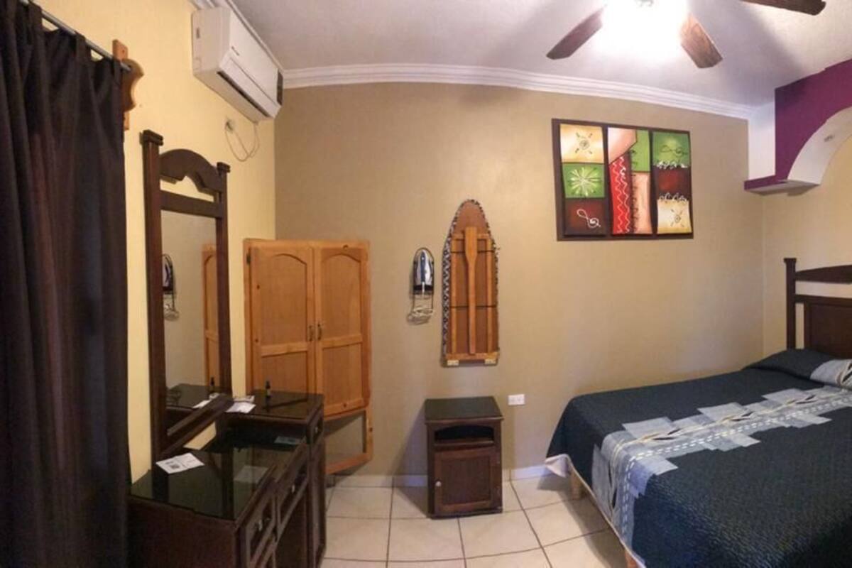 Un dormitorio con cama, cómoda, espejo, una mesita y aire acondicionado instalado en la pared.