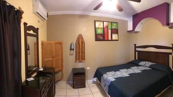 Un dormitorio con cama, cómoda, espejo, una mesita y aire acondicionado instalado en la pared.