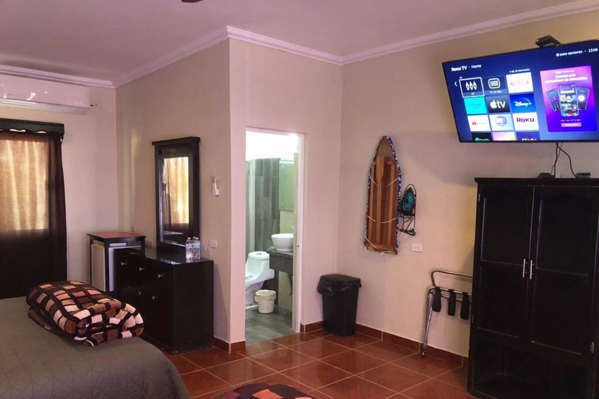 Habitación de hotel con cama, televisor montado en la pared, armario y baño visible a través de una puerta abierta.