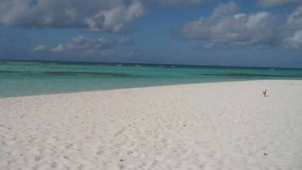 Una playa de arena blanca y agua turquesa bajo un cielo parcialmente nublado.