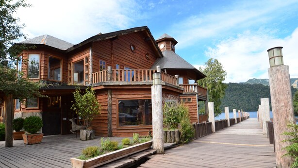 A wooden cabin with a balcony, a dock extending to a body of water, and a mountainous backdrop. - Huilo Huilo Marina del Fuy (Panguipulli)