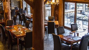 A restaurant with wooden tables and chairs, stone walls, and a view of the outdoor patio. - Huilo Huilo Marina del Fuy (Panguipulli)