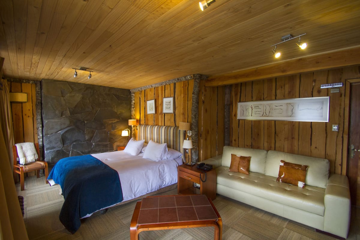 A wooden-paneled room with a bed, a sofa, a coffee table, and a stone wall.