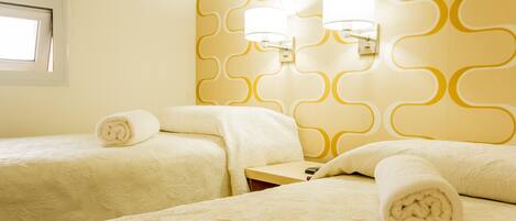 A hotel room with two beds, each with a rolled towel, a nightstand, and wall-mounted lamps.