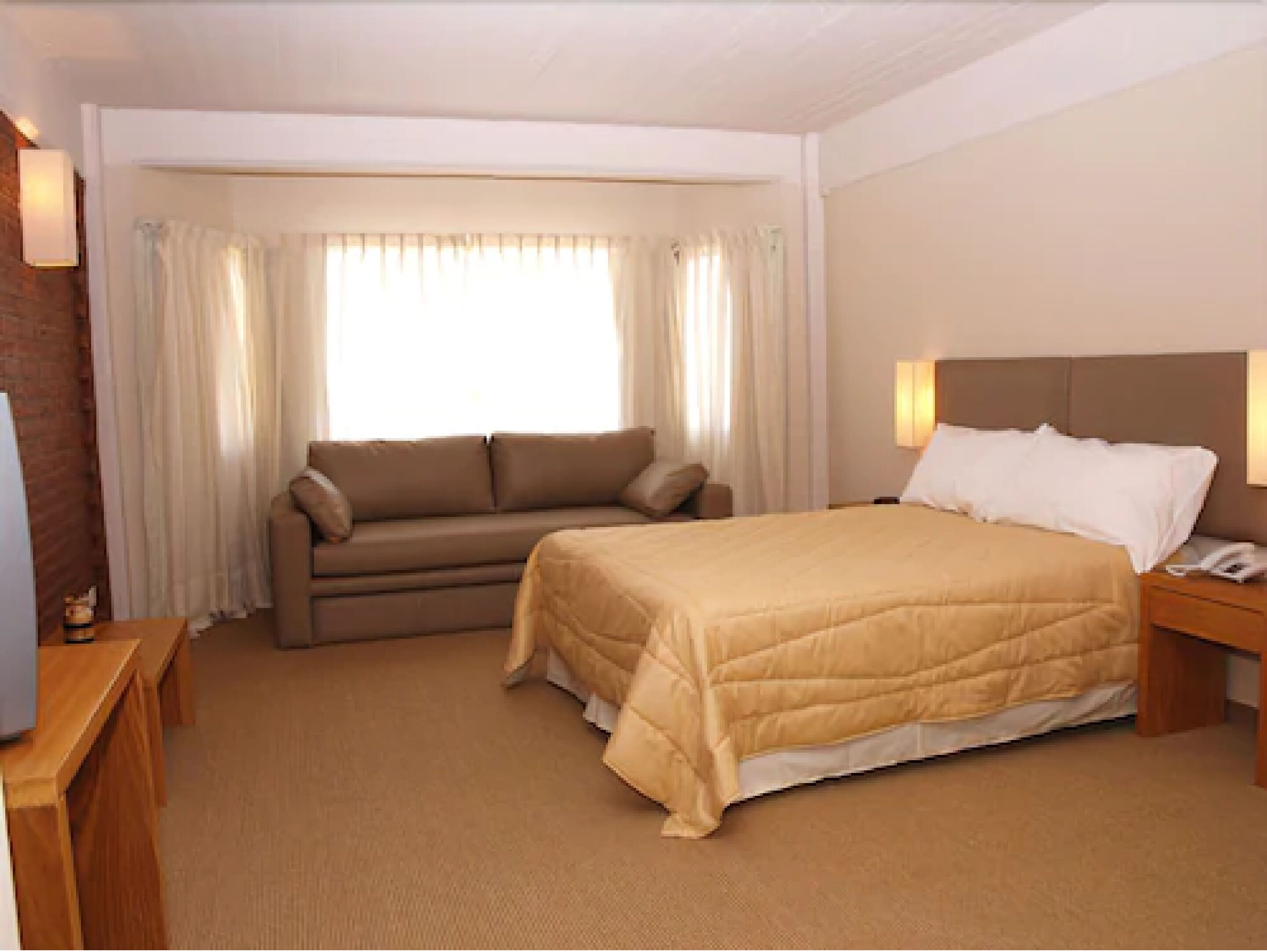 A hotel room with a bed, a sofa, a desk, and a window with curtains.