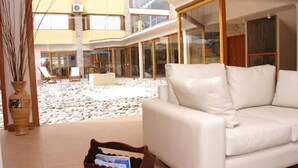 Amplia sala de estar con un sofá de cuero blanco, un amplio ventanal con acceso a un balcón y suelo de piedra.