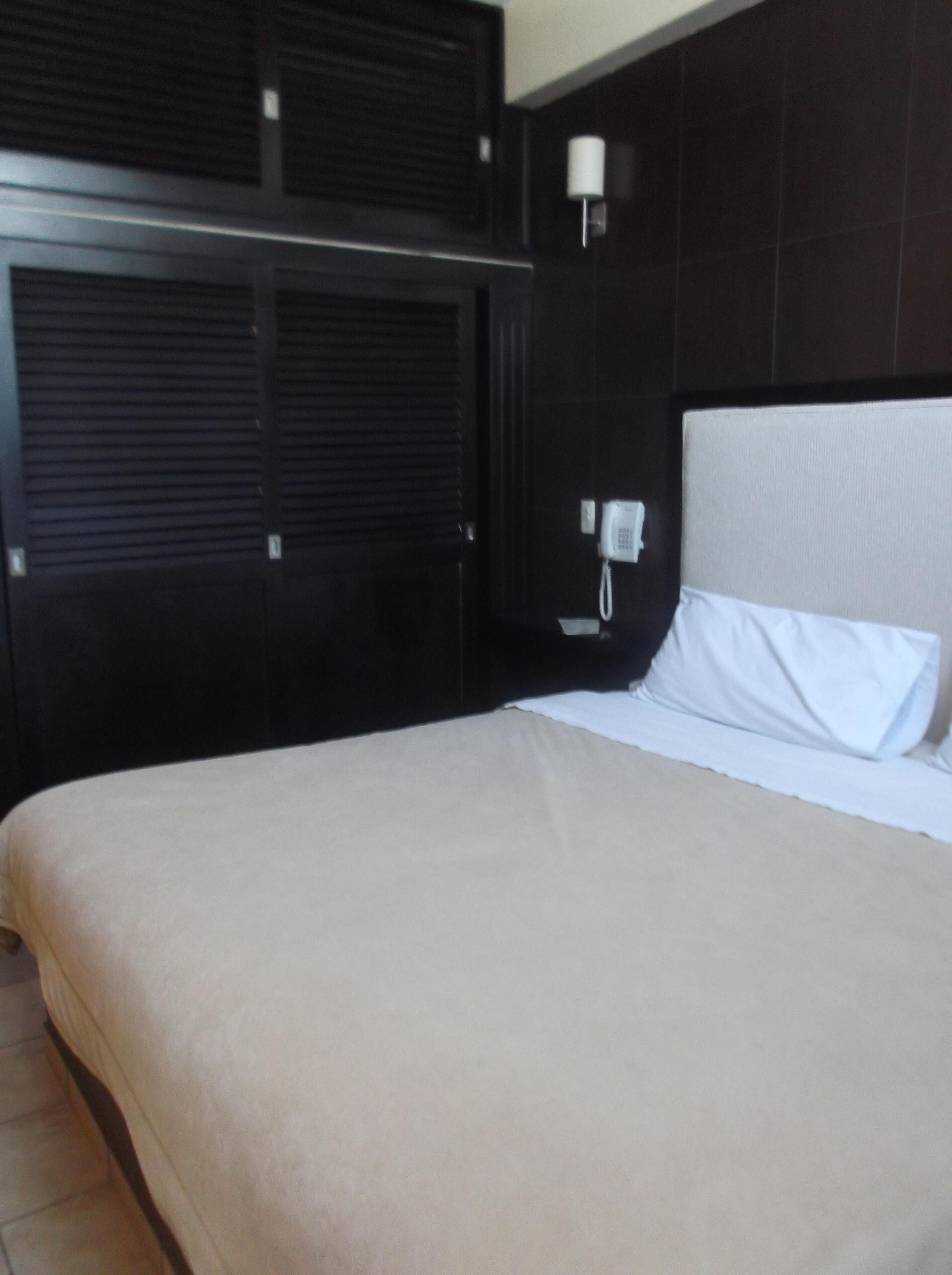 A hotel room with a large bed, a bedside telephone, and a wall-mounted light fixture.