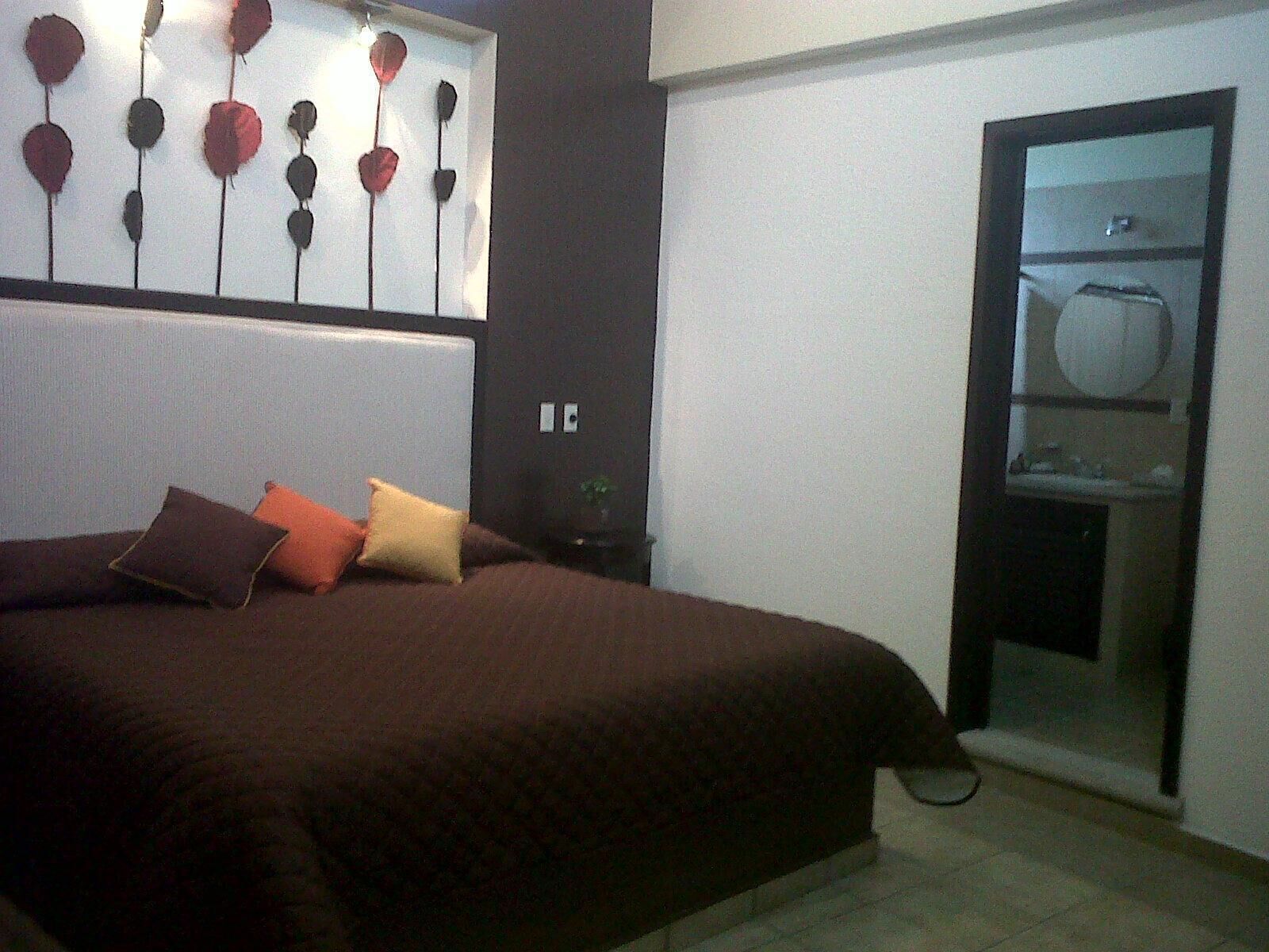A bedroom with a large bed, a wall-mounted light fixture, and a door leading to a bathroom.