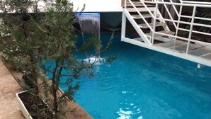 Una piscina con una cascada, rodeada por una cerca blanca y un macetero con follaje.