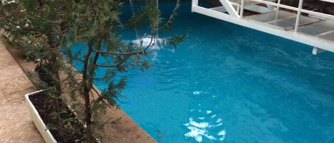 Una piscina con una cascada, rodeada por una cerca blanca y un macetero con follaje.
