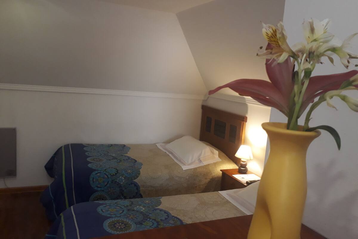 Ein Schlafzimmer mit einem Bett, einem Nachttisch, einer Lampe und einer Vase mit Blumen.