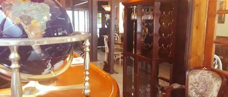 Una zona de bar con barra de madera, un globo terráqueo, un armario con cristalería y una silla estampada.