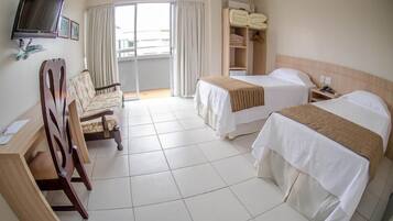 Quarto de hotel com duas camas, uma escrivaninha, uma cadeira, uma televisão e uma janela com cortinas.