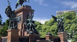Une statue représentant un homme brandissant une épée, monté sur un cheval, et entourée d’autres statues et de verdure.