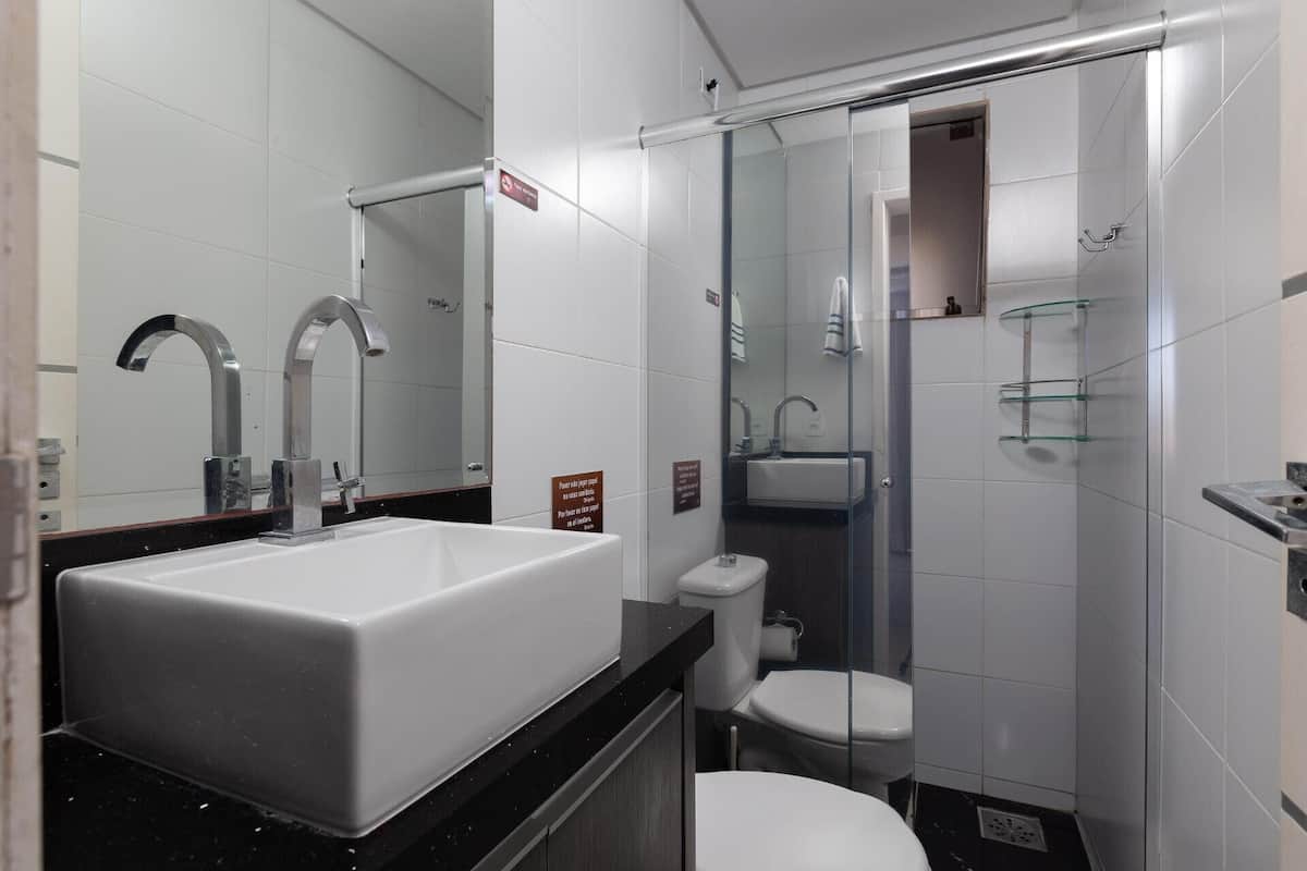 Une salle de bain moderne avec un grand lavabo blanc, deux robinets, une douche en verre et des toilettes.