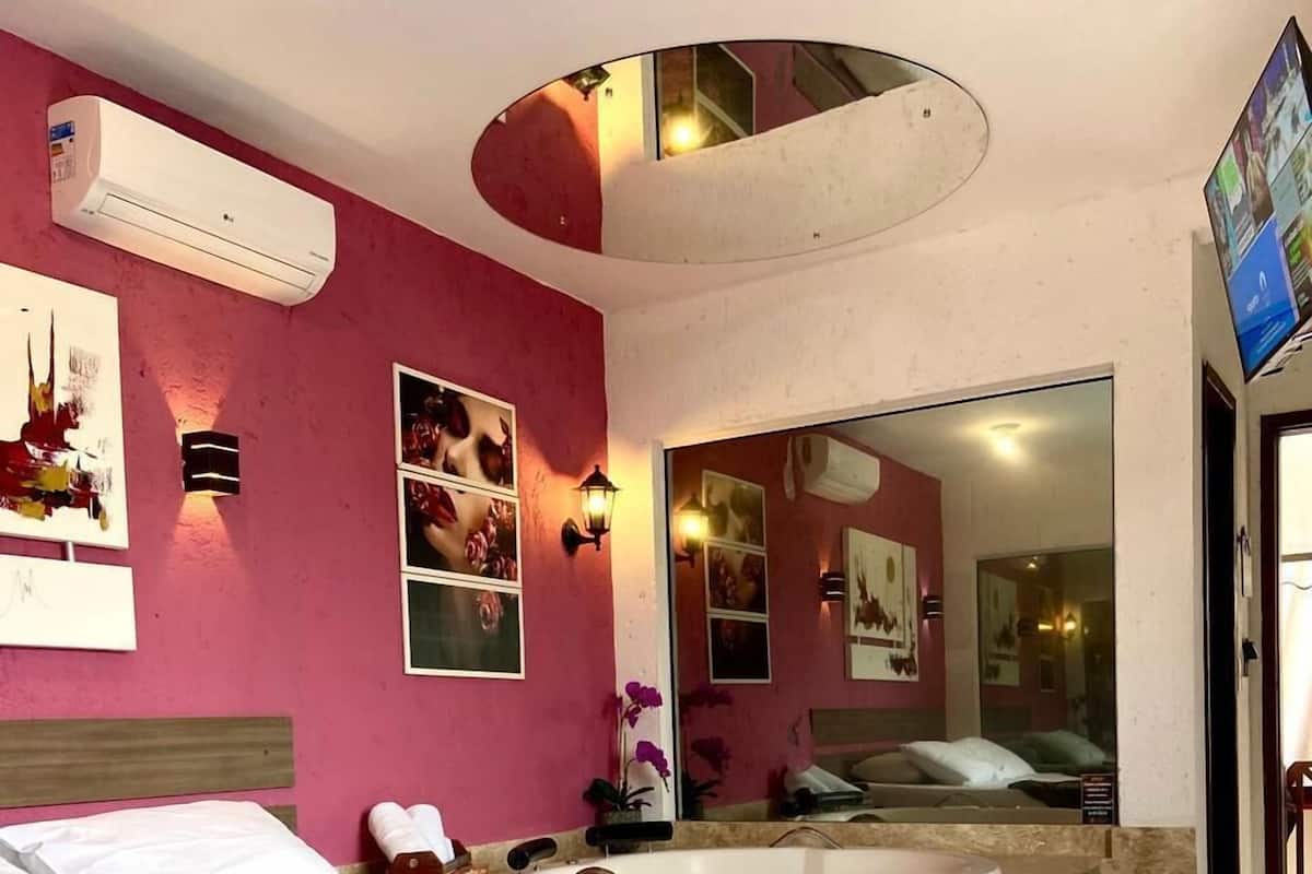 Une chambre d’hôtel avec un lit, un grand miroir, une baignoire et un téléviseur.