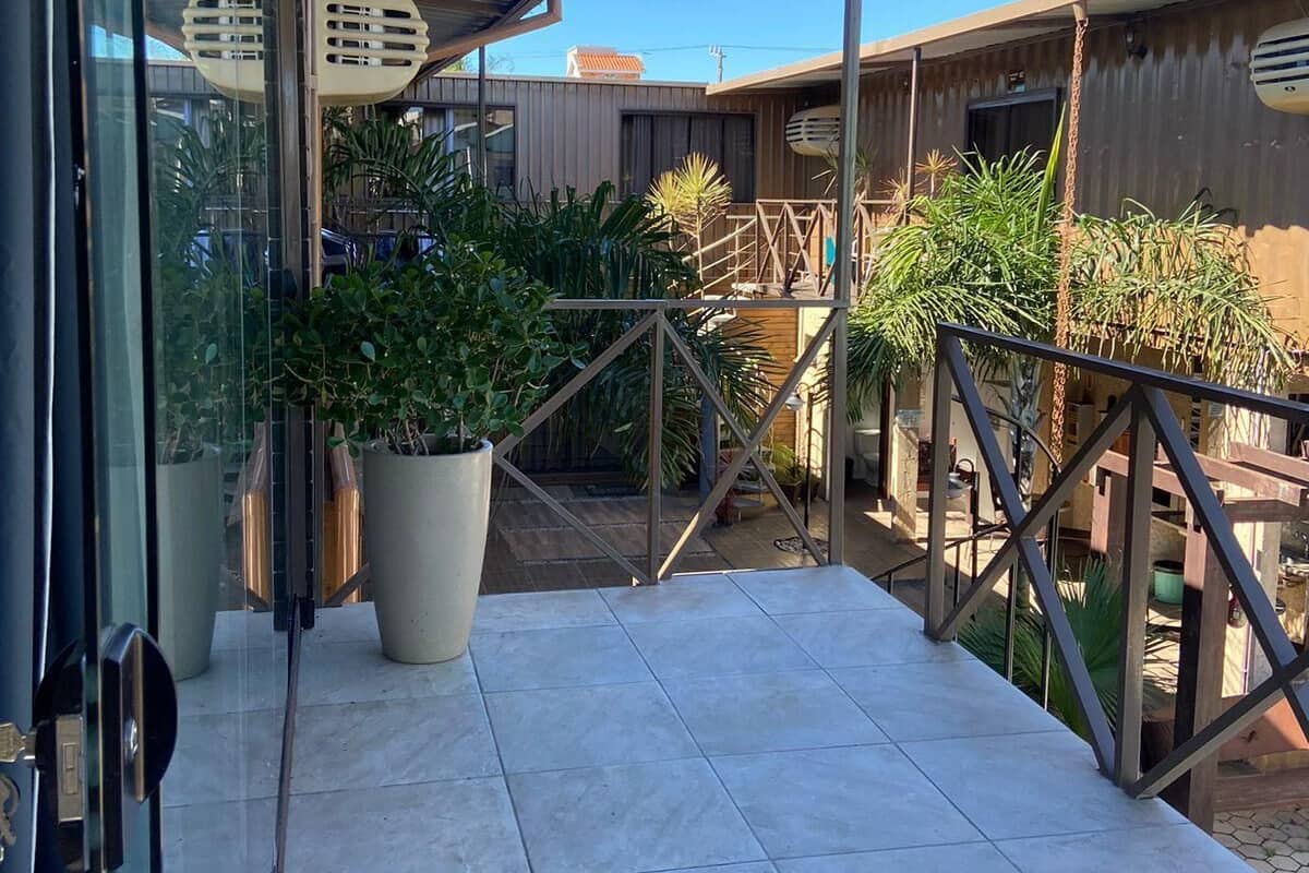 Un balcon fermé, agrémenté de plantes en pot, doté d’une rambarde en métal et offrant une vue sur un bâtiment situé au loin.