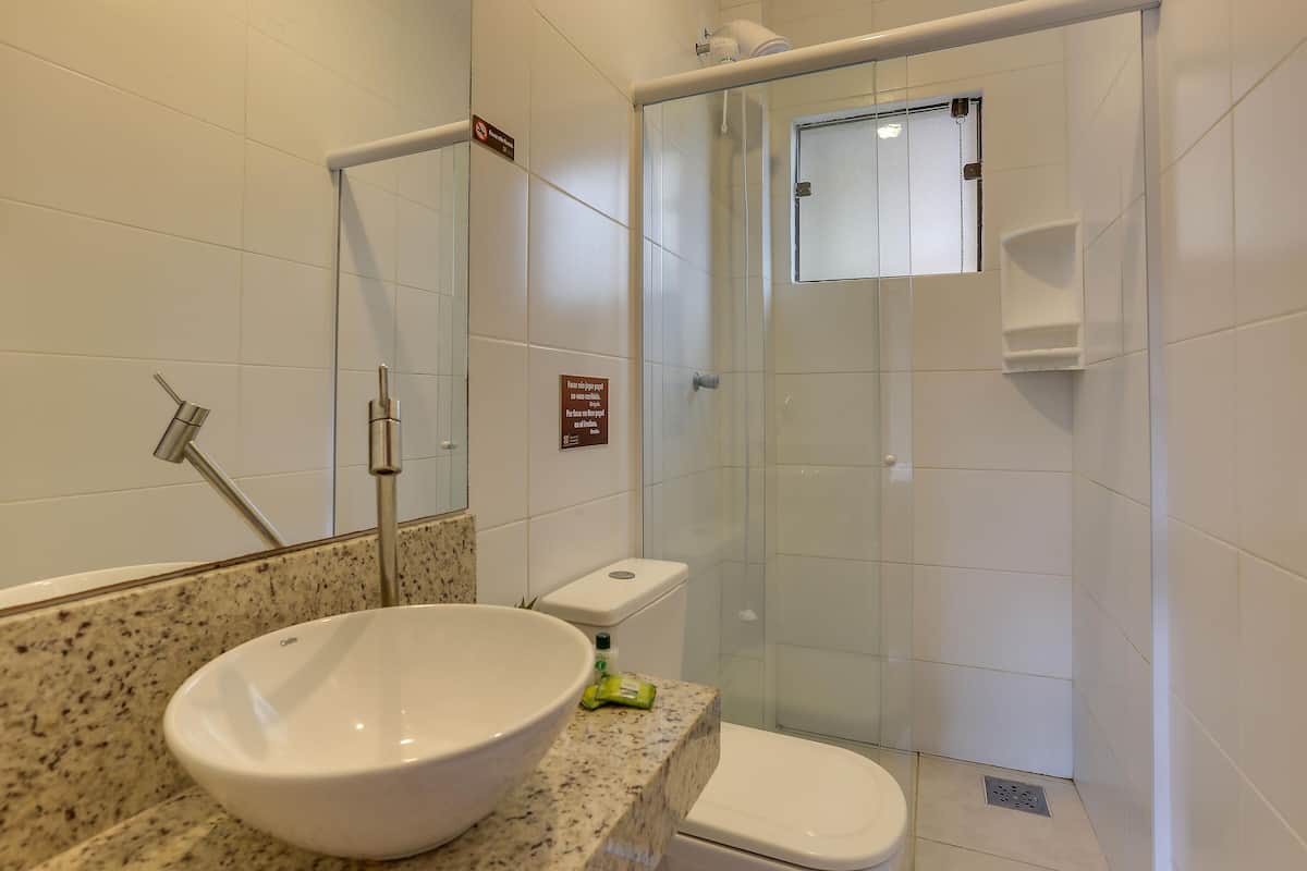 Une salle de bain avec un grand lavabo blanc, une douche en verre et des toilettes.